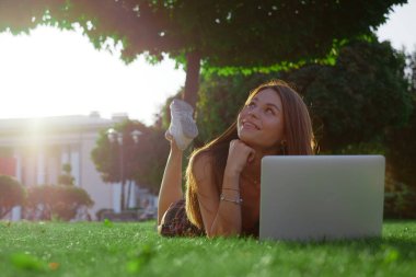 Parkta yeşil çimlerin üzerinde dizüstü bilgisayar kullanan genç bir kadın. Boş zaman aktivite kavramı. 