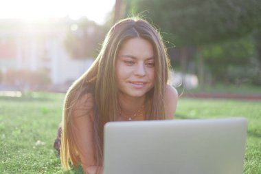 Parkta yeşil çimlerin üzerinde dizüstü bilgisayar kullanan genç bir kadın. Boş zaman aktivite kavramı. 