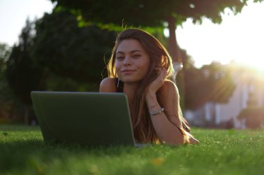 Parkta yeşil çimlerin üzerinde dizüstü bilgisayar kullanan genç bir kadın. Boş zaman aktivite kavramı. 
