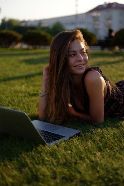 Parkta yeşil çimlerin üzerinde dizüstü bilgisayar kullanan genç bir kadın. Boş zaman aktivite kavramı. 