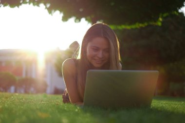 Parkta yeşil çimlerin üzerinde dizüstü bilgisayar kullanan genç bir kadın. Boş zaman aktivite kavramı. 