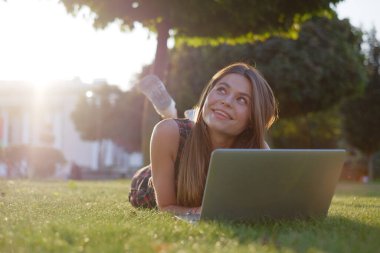 Parkta yeşil çimlerin üzerinde dizüstü bilgisayar kullanan genç bir kadın. Boş zaman aktivite kavramı. 