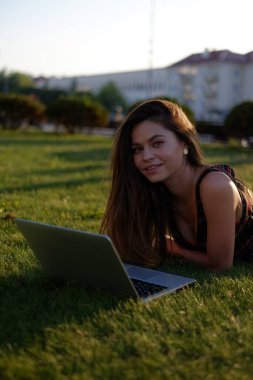 Parkta yeşil çimlerin üzerinde dizüstü bilgisayar kullanan genç bir kadın. Boş zaman aktivite kavramı. 