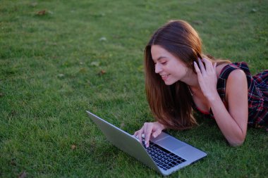 Parkta yeşil çimlerin üzerinde dizüstü bilgisayar kullanan genç bir kadın. Boş zaman aktivite kavramı. 