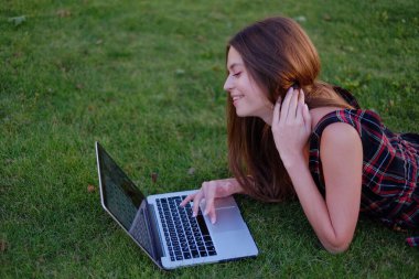 Parkta yeşil çimlerin üzerinde dizüstü bilgisayar kullanan genç bir kadın. Boş zaman aktivite kavramı. 