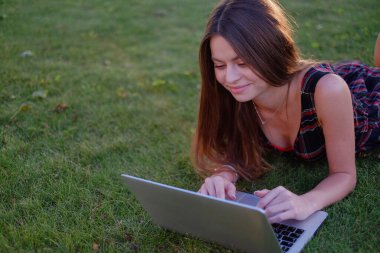 Parkta yeşil çimlerin üzerinde dizüstü bilgisayar kullanan genç bir kadın. Boş zaman aktivite kavramı. 