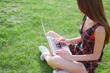 Parkta yeşil çimlerin üzerinde dizüstü bilgisayar kullanan genç bir kadın. Boş zaman aktivite kavramı. 