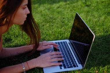 Parkta yeşil çimlerin üzerinde dizüstü bilgisayar kullanan genç bir kadın. Boş zaman aktivite kavramı. 