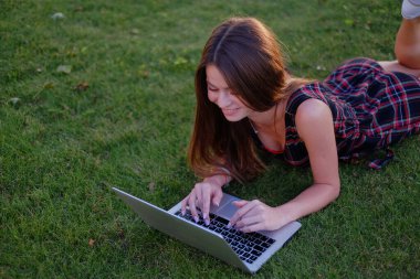 Parkta yeşil çimlerin üzerinde dizüstü bilgisayar kullanan genç bir kadın. Boş zaman aktivite kavramı. 