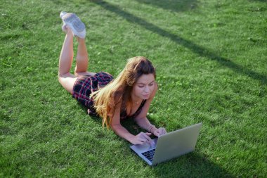 Parkta yeşil çimlerin üzerinde dizüstü bilgisayar kullanan genç bir kadın. Boş zaman aktivite kavramı. 