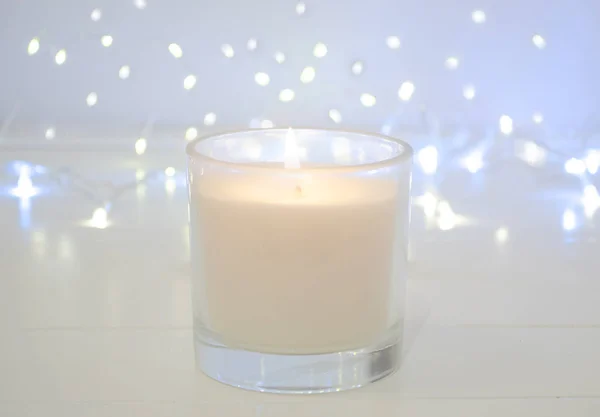White candle on white background with bokeh lights. Christmas concept. Copy space. Simple minimalism concept. Candle flame at night with bokeh. Abstract blurred background.