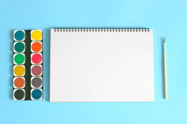 Sanat konsepti. Okula dönelim. Mavi arkaplanda beyaz defter ve fırça ile suluboya. 