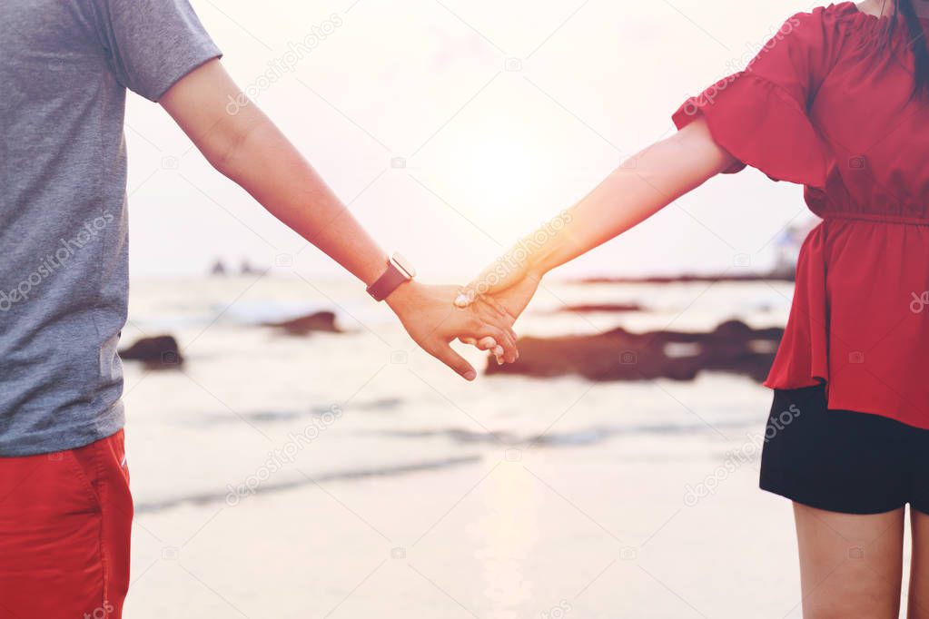 couple hand hold together on the beach with sunset.