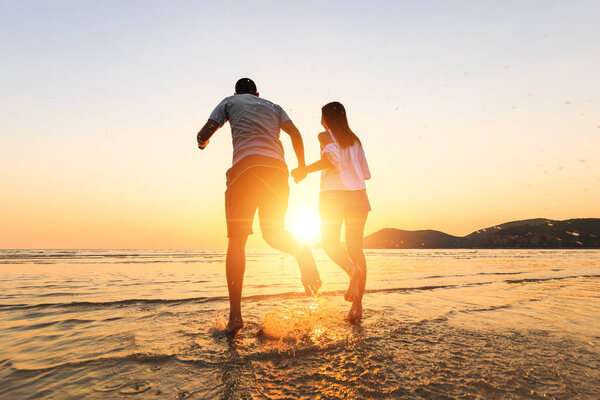 пара бежит и держатся за руки на пляже между закатом
.