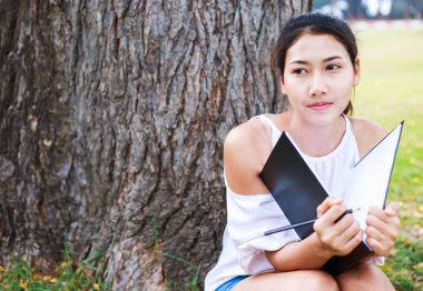 Büyük ağacın yanında oturan ve parkta çizim kadın.