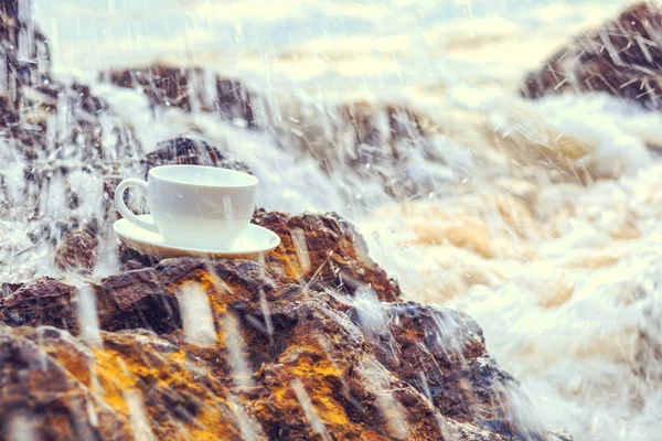 A cup of coffee on the stone in the beach and water splash.