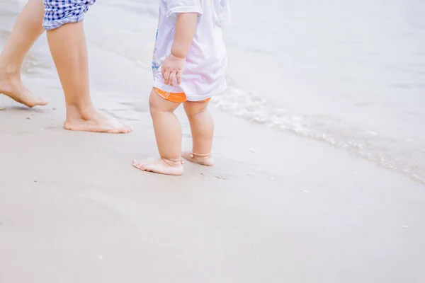 Mother and baby feet walking on a sand beach.