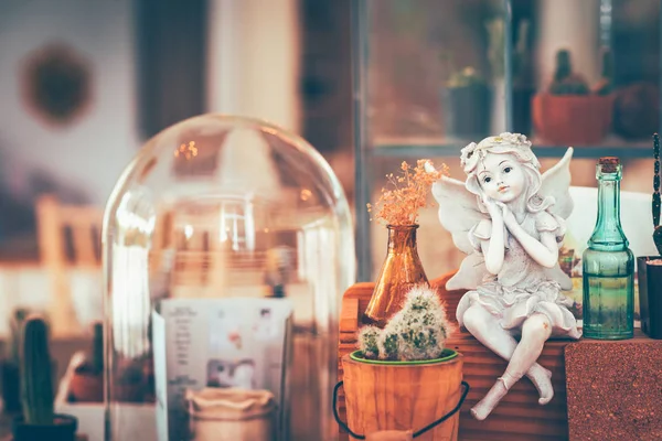 灰泥丘比特罗马娃娃坐在小木箱附近的仙人掌在咖啡店 — 图库照片