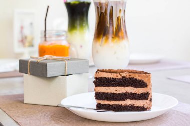 masada hediye kutusunun yanındaki masada çanak çikolatalı kek ve çatal parçası.