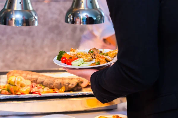 A steak pork, tomato, vegetable are in the dish. A man hold dish in the restaurant.