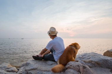 Denize yakın bir taşın üzerinde birlikte oturan bir adam ve bir köpek