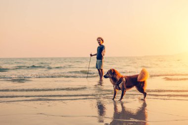Bir adam ve bir köpek sahilde ve gün batımında, gün doğumunda.
