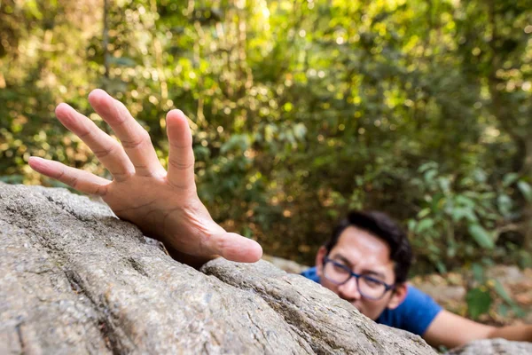 A man climb rock in the forest and hand for help.