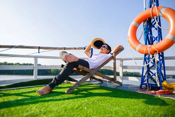 一个男人戴着帽子 戴着太阳镜 他躺在游轮上的日光浴床上 — 图库照片