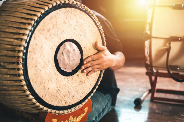 Asian male hit a two-faced drum to make music.