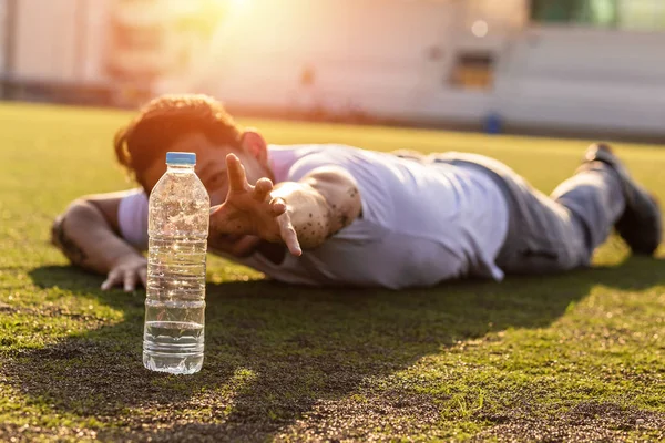Spor stadyumunda çim üzerinde Susamış adam saf su bir şişe ulaşmak.