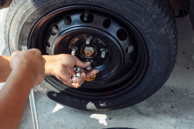 Tamircinin elleri araba tekerleğinin somunu alır. Lastik bakım, hasarlı araba lastiği ile otoparkta düz bir araba lastiği değiştirin.