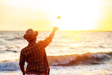 Adam gün batımında deniz suyuna taş atıyor..