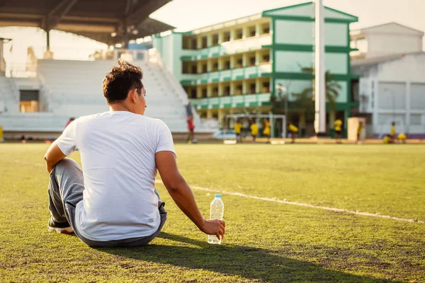 スポーツスタジアムの草の上ののどが渇いた男と手は純水のボトルをキャッチ — ストック写真