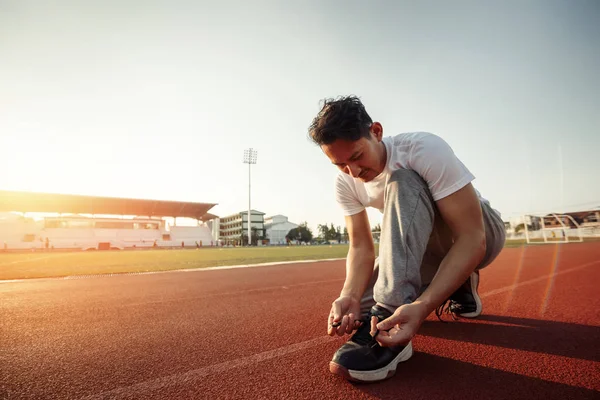 çekici esmer adam parça yarışında onu spor ayakkabı enlacing. Gün batımı ile spor stadyumunda bir adam.