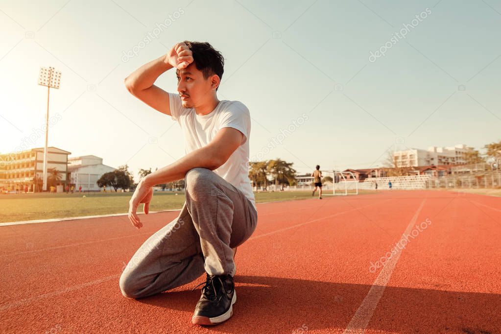 Tired wet athletic man wiping sweat his hand at sport stadium with sunset.