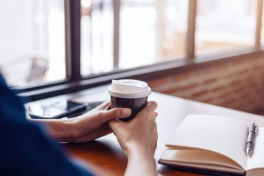 Genç kız ve bir fincan sıcak kahve. Kitap, kalem ve tablet masanın üzerinde..