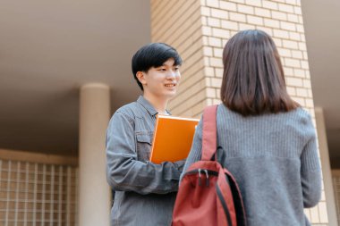 Lise öğrencileri ders aralarında kitap ve dizüstü bilgisayarla konuşup gülüyorlar.
