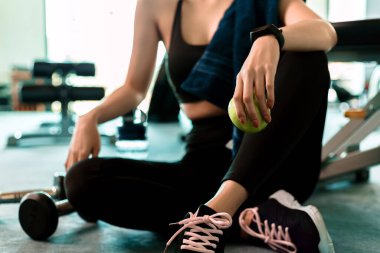 Spor salonundaki kadın egzersizi ara verip rahatlıyor. Spor ve dambıl eğitiminden sonra elmanın meyvesini tutarken yerde su şişesi..