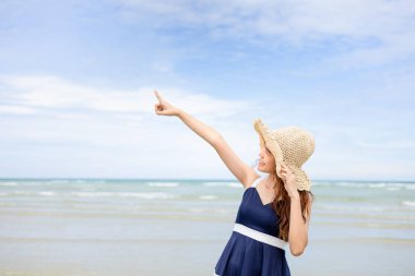 Kadın şapkası ve el işareti yaz mevsiminde deniz suyu ve kumsaldaki kum dalgaları boyunca gökyüzünü gösteriyor.. 
