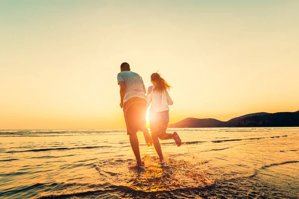 幸せなカップルが走っていて 日没の間にビーチで手を握っています カップル新婚旅行のコンセプト — ストック写真
