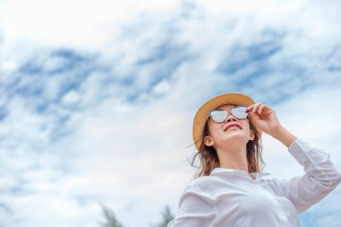 Güneş şapkalı ve kumsalda güneş gözlüklü gülümseyen genç bir kadın. yaz, tatiller, tatil, seyahat kavramı