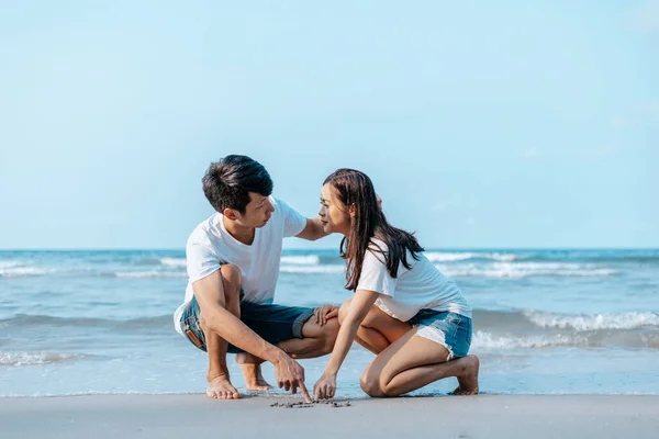 ロマンチックなカップルはビーチで砂の中にハートの形を描きます — ストック写真