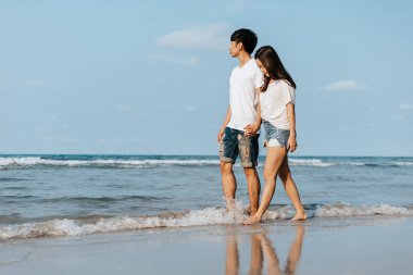 Romantik çift el ele tutuşup sahilde yürüyor. Aşık bir adam ve kadın.