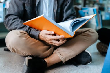 Öğrenci üniversitesi kütüphanede bir kitap açıyor ve okuyor.