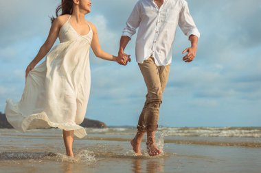 Genç çift el ele tutuşup sahilde koşuyor..