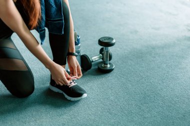 Spor salonunda ayakkabı bağcıklarını bağlayan kadın elleri. Dambıl ve su şişesi kızın etrafında yerde..