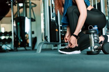 Spor salonunda ayakkabı bağcıklarını bağlayan kadın elleri. Dambıl ve su şişesi kızın etrafında yerde..