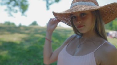 modern hasır şapkalı oturan ve çim çim üzerinde poz çekici sarışın Bayan 