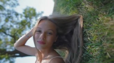 slow motion düşük açılı yan sarı uzun saçlı kızı vuran arkasına düşüyor ve gölgeli bir yerde çim üzerinde yalan