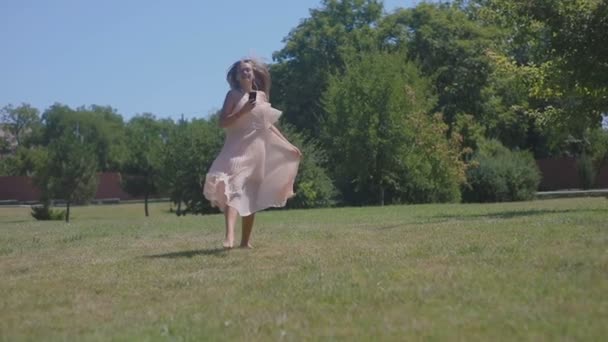 スローモーション金髪長い髪の女の子の裸足が暑い日に夏の公園で音楽回転とスカート ファンに踊りを実行します — ストック動画